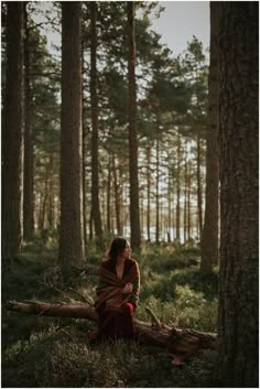 a woman sitting on top of a log in the middle of a forest filled with trees