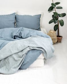 a bed with blue sheets and pillows on top of it next to a potted plant