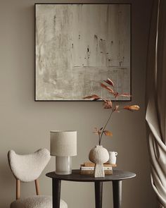 a table with two chairs and a vase on it in front of a framed art piece