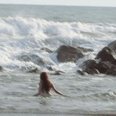 a woman sitting in the ocean with her back to the camera, looking out at the waves