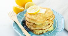 a stack of pancakes with butter and blueberries on a plate next to lemon wedges