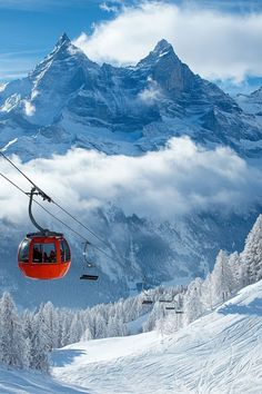 a red ski lift going up the side of a snow covered mountain filled with trees