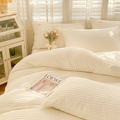 a bed with white comforters and pillows in a bedroom next to a book shelf