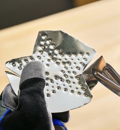 a close up of a person's hand holding a metal spatula with holes on it