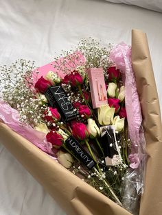 a bouquet of roses and lipstick in a brown paper box on a white bed sheet