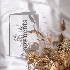 two books sitting on top of a bed next to dried flowers and leaves in front of them