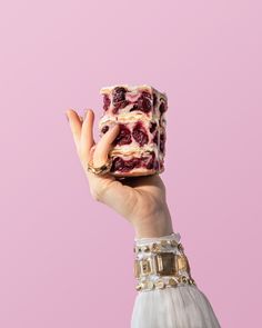 a woman holding up a piece of cake with berries on it in front of a pink background