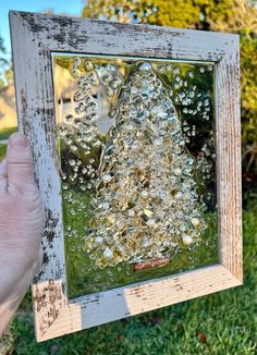 a person holding up an old window with water droplets on the glass and grass behind it