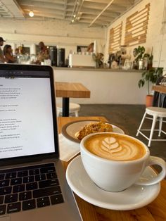 a laptop computer sitting on top of a wooden table next to a cup of coffee