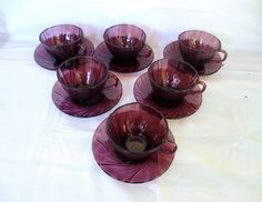 six purple glass cups and saucers on a white tablecloth