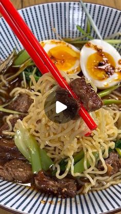 a bowl filled with noodles, meat and veggies next to chopsticks