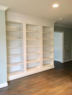 an empty room with white bookcases and hard wood flooring in the middle