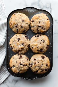 freshly baked chocolate chip muffins on a black tray with a white towel next to it