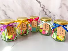 four small glass jars filled with colorful sticky notes and tied with ribbons, sitting on a marble surface