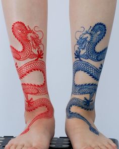 two legs with red and blue dragon tattoos on their ankles, one is sitting on a keyboard