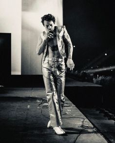 a man walking down a runway while holding a cell phone to his ear and wearing silver pants