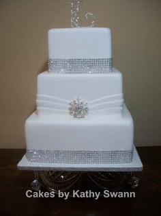 a three tiered white wedding cake with a diamond decoration on the top and bottom