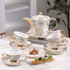 tea set with matching saucers, cups and plates on a table in front of a book