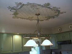 a chandelier hanging from the ceiling in a kitchen with green cabinets and white counter tops