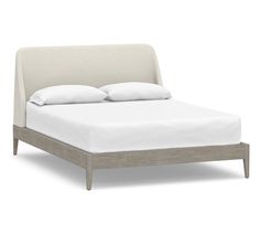 an upholstered bed with white sheets and pillows