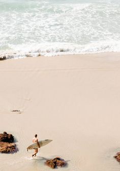 a man walking on the beach with a surfboard in his hand and footprints in the sand