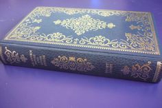 a blue book with gold trim sitting on top of a purple table