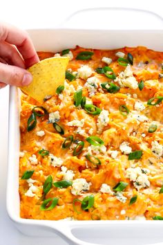 a hand dipping a tortilla chip into a casserole dish