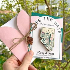 someone is holding up a pink and green save the date card with a pine cone on it