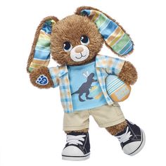 a brown stuffed animal wearing a blue shirt and tan pants with an egg in it's hand