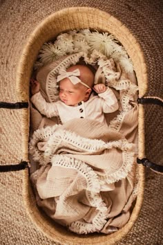 a baby is laying in a basket with white flowers on the bottom and headbands