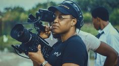 a woman with headphones on holding a camera in front of her face and another man behind her