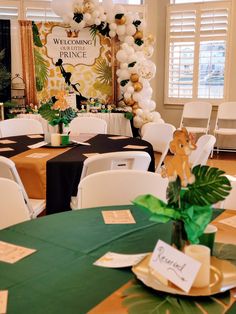 a room filled with tables and chairs covered in green table cloths, white balloons and jungle decorations