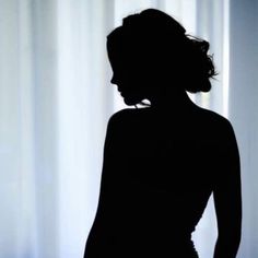 the silhouette of a woman standing in front of curtains