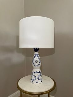 a blue and white table lamp sitting on top of a wooden stand next to a wall