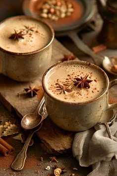 two mugs filled with hot chocolate on top of a wooden table next to cinnamon sticks