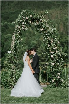 a bride and groom kissing in front of a floral arch