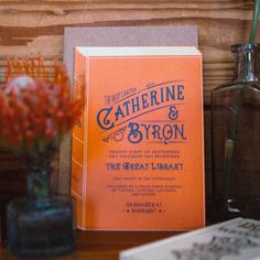 an orange book sitting on top of a table next to a vase filled with flowers