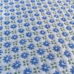 blue and green flowers on white fabric with small dots in the center, closeup