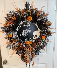 a halloween wreath on the front door decorated with black and orange ribbons, skulls, and pumpkins