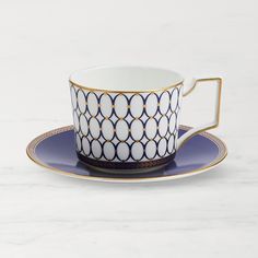 a cup and saucer sitting on top of a white marble countertop with gold trimming