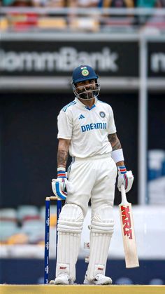 a man standing on top of a cricket field holding a bat and wearing a helmet