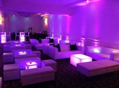 a room filled with lots of white couches and chairs covered in purple lights at night