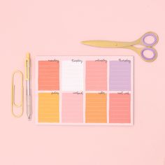 a pink and yellow planner with scissors next to it on a pink surface, surrounded by other office supplies