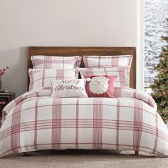 a red and white plaid comforter set on a bed with christmas tree in the background