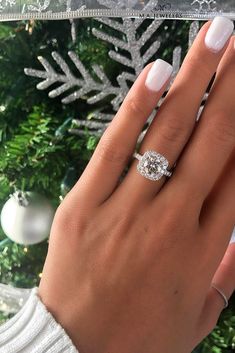 a woman's hand with a ring on her finger next to a christmas tree