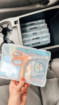 a person holding a plastic container filled with scissors and other items in the back seat of a car