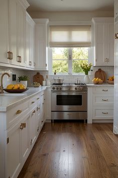 a kitchen with white cabinets and wood floors is pictured in this image, there are fruit on the counter