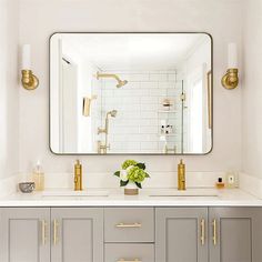 a white bathroom with gold accents and mirrors on the wall, along with gray cabinets