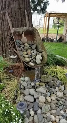 a water feature in the middle of a garden with rocks and plants around it, next to a tree