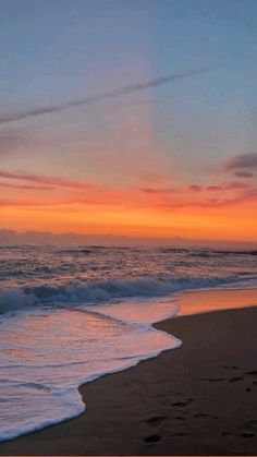 the sun is setting at the beach with waves coming in